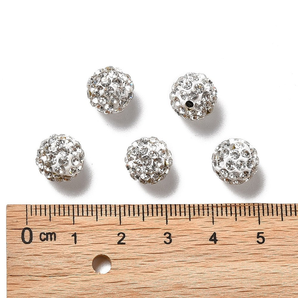 five loose pave clear rhinestone clay beads displayed above wooden ruler over white background. 