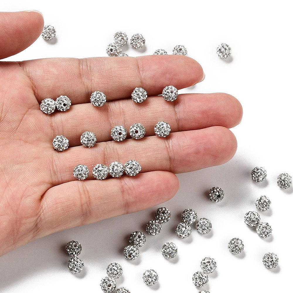 loose pave clear rhinestone clay beads displayed in a hand and spread around the white surface below.