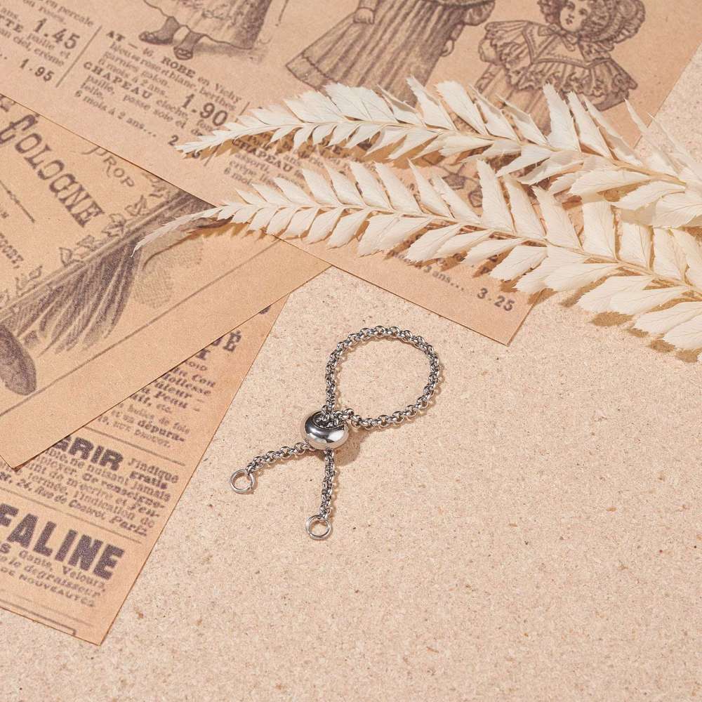 silver tone adjustable fidget ring with Rolo chain and slider bead and two jump rings over light brown textured surface with old newspaper articles and dried flowers in the top corners. 