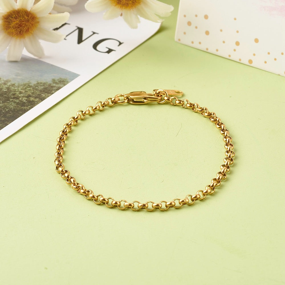 golden rolo chain with lobster claw clasp and extender tab displayed on light green surface with a magazine, some white flowers and a white and gold box peeking in from the top. 