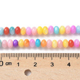 two strands of multi-color dyed shell rondelle beads displayed above wooden ruler on white background. 