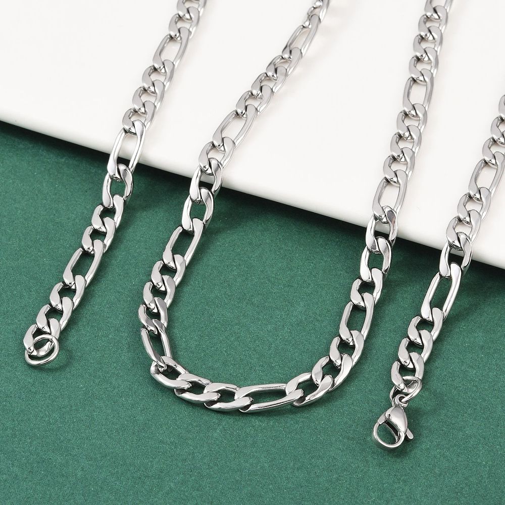 silver tone Figaro chain necklace with lobster claw clasp draped over a white ledge onto a green felt surface.