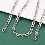 silver tone Figaro chain necklace with lobster claw clasp draped over a white ledge onto a green felt surface.