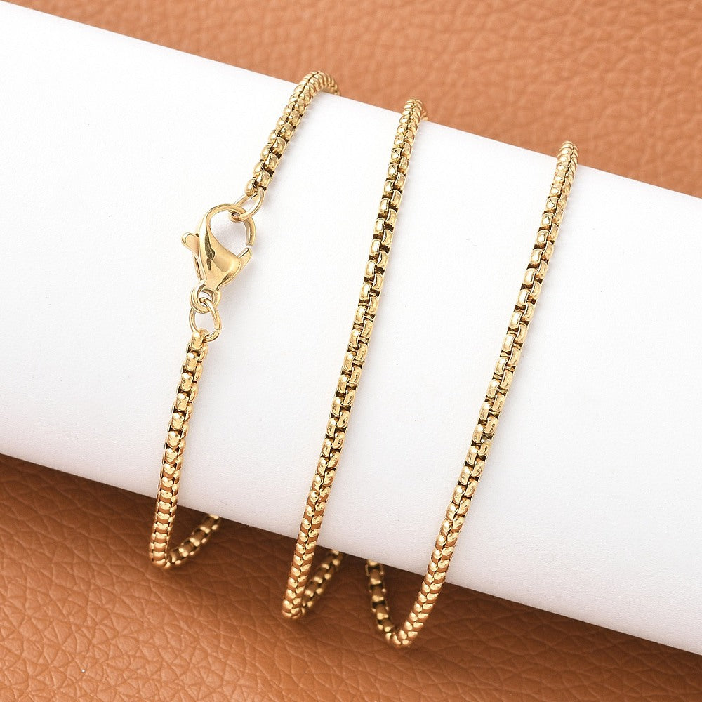 golden Venetian box chain with lobster claw clasp wrapped around a white cylinder over an orange leather surface. 