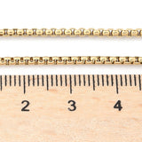 golden Venetian box chain displayed above wooden ruler on white background. 