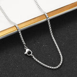 silver tone Venetian box chain with lobster claw clasp draped over a ledge onto a black textured surface. 
