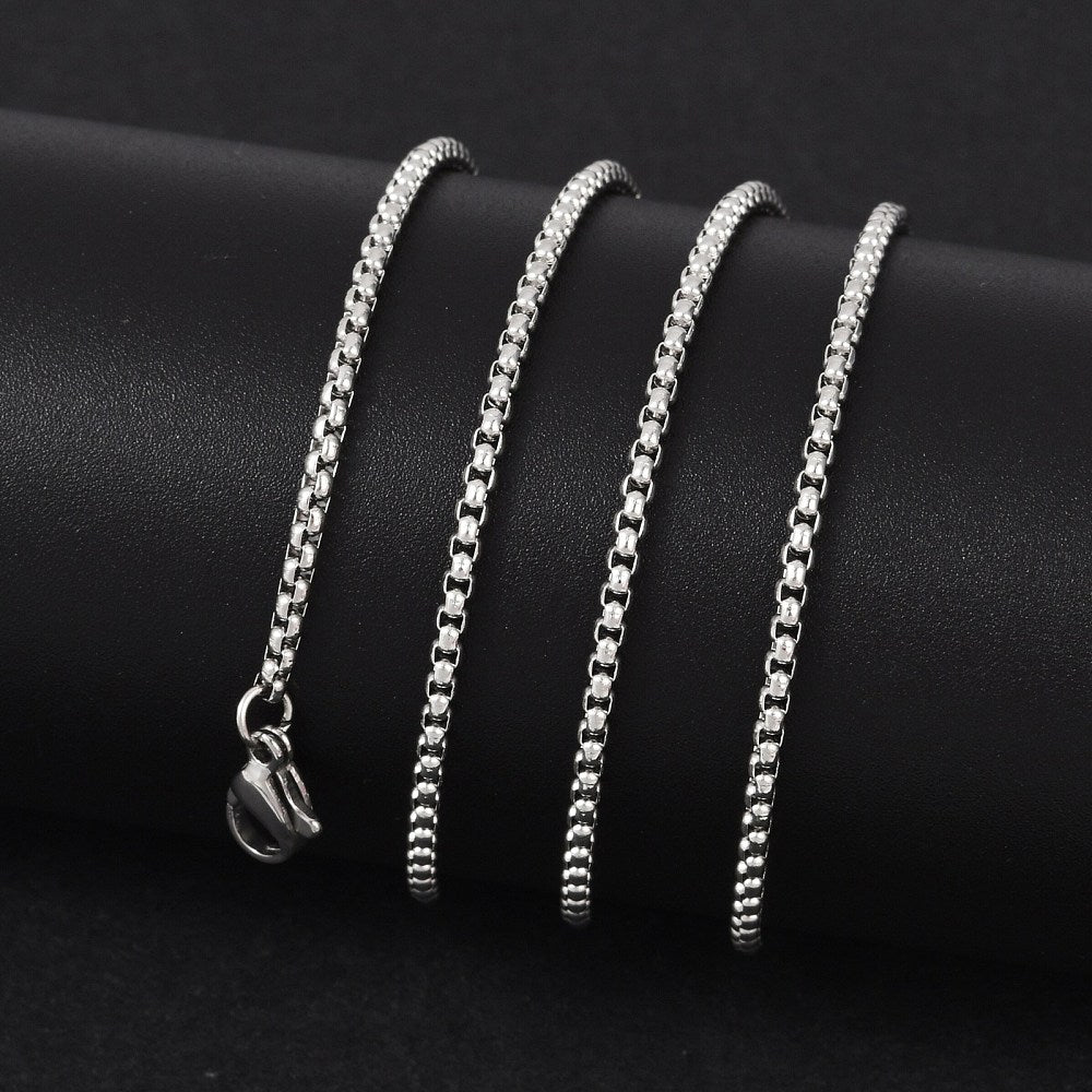 silver tone Venetian box chain with lobster claw clasp wrapped around a black cylinder on black background.  