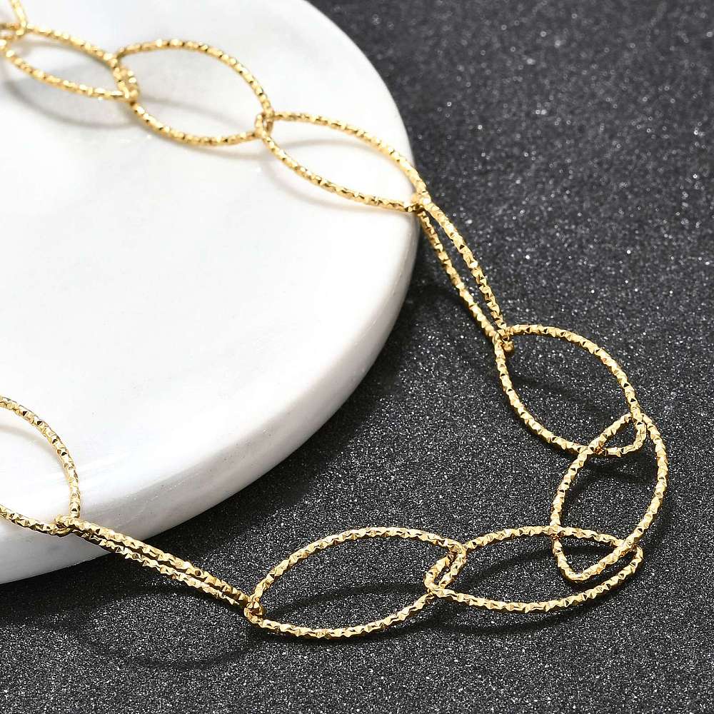 zoomed in section of golden textured horse eye link necklace draped over white ledge onto black textured surface.  