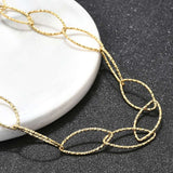 zoomed in section of golden textured horse eye link necklace draped over white ledge onto black textured surface.  