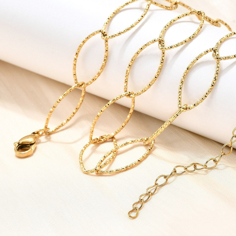 golden textured horse eye link necklace with lobster claw clasp and extender chain draped over a white ledge onto a cream surface. 