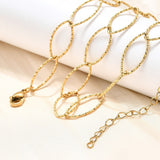 golden textured horse eye link necklace with lobster claw clasp and extender chain draped over a white ledge onto a cream surface. 