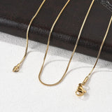 golden square snake chain with lobster claw clasp draped over black leather folder onto a white textured surface. 