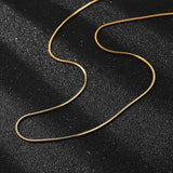golden square snake chain necklace on black textured background. 