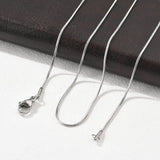 silver tone square snake chain with lobster claw clasp draped over black leather folder onto a white textured surface. 