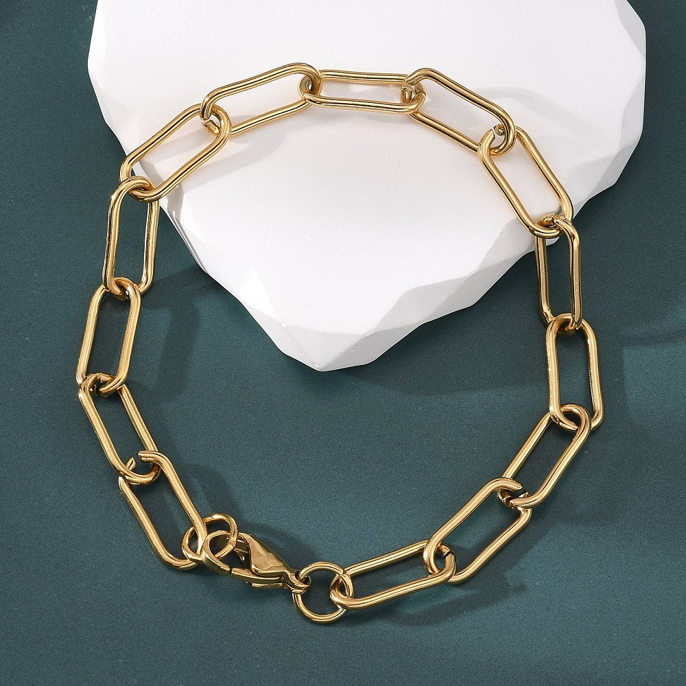 golden rounded paperclip chain bracelet with lobster claw clasp  draped over a white rock on a green felt background. 