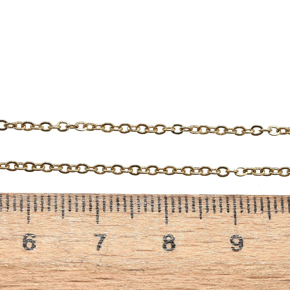 golden fine flat cable chain necklace displayed above a wooden ruler on a white background. 