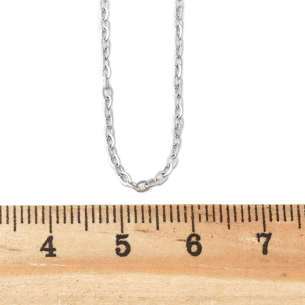 silver tone fine flat cable chain necklace displayed above a wooden ruler on a white background. 