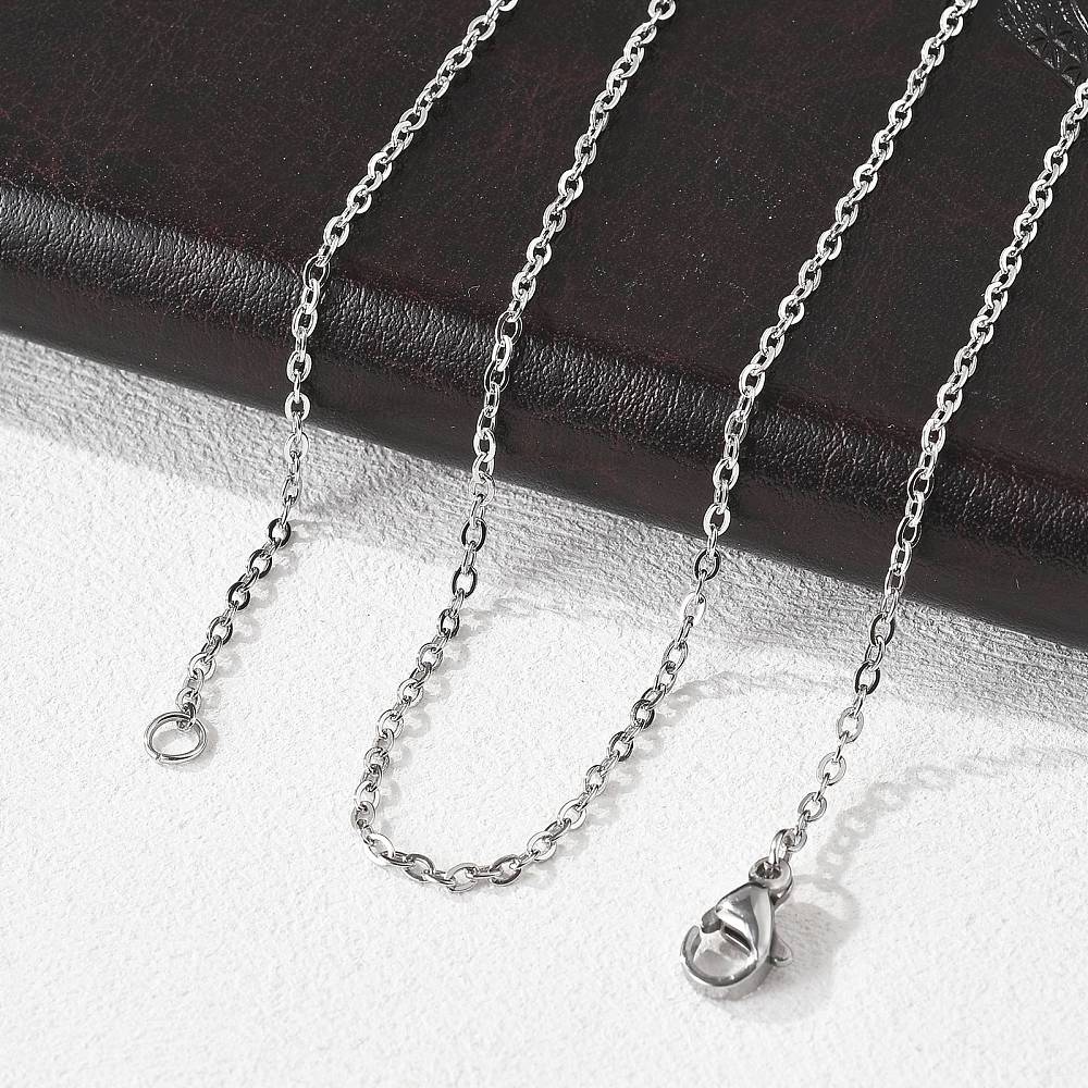 silver tone fine flat cable chain necklace with lobster claw clasp draped over a black leather pad onto a white textured surface. 