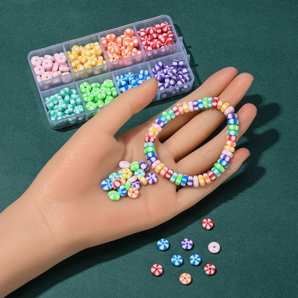 plastic bead box sectioned with eight different color candy swirl beads and samples of the beads loose and strung are on display on a mannequin hand and on the green felt surface. 