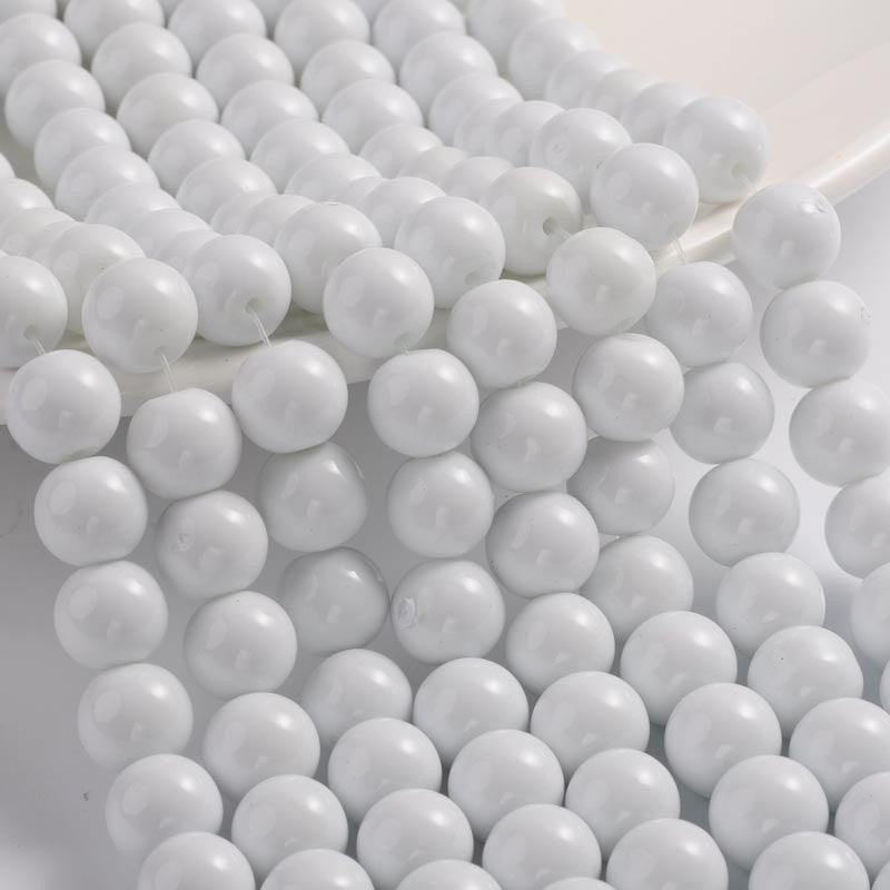 smooth round white opaque glass bead strands draped over white tray ledge onto a white surface. 