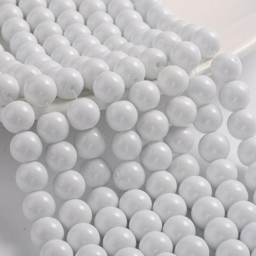 smooth round white opaque glass bead strands draped over white tray ledge onto a white surface. 