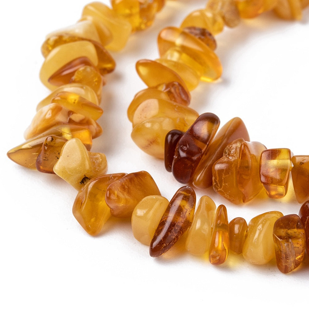 zoomed in sections of mixed color natural amber chip bead strand over white surface. 