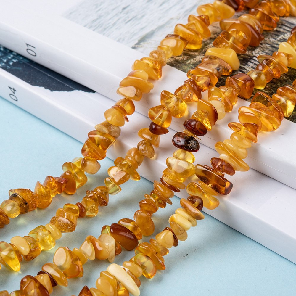 mixed color natural amber chip bead strands draped over two magazines onto a light blue surface.