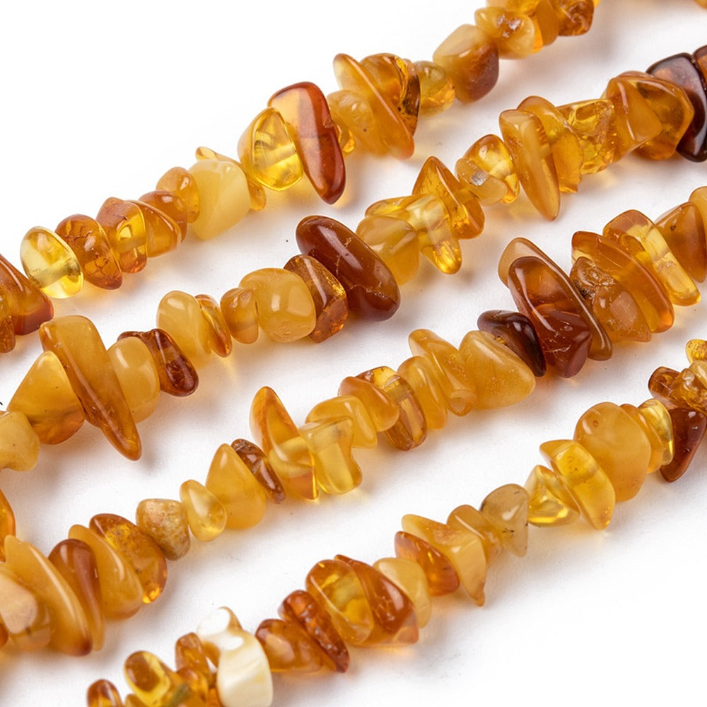 zoomed in sections of mixed color natural amber chip bead strand over white surface. 