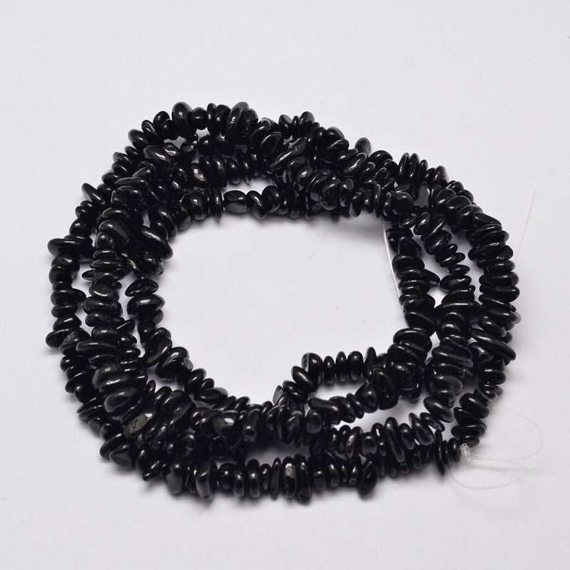 black tourmaline stone chip strands in a swirl design over white background. 