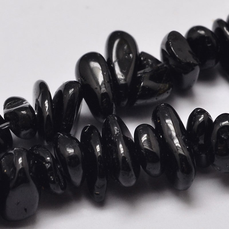 zoomed in sections of black tourmaline chip strand over white background. 