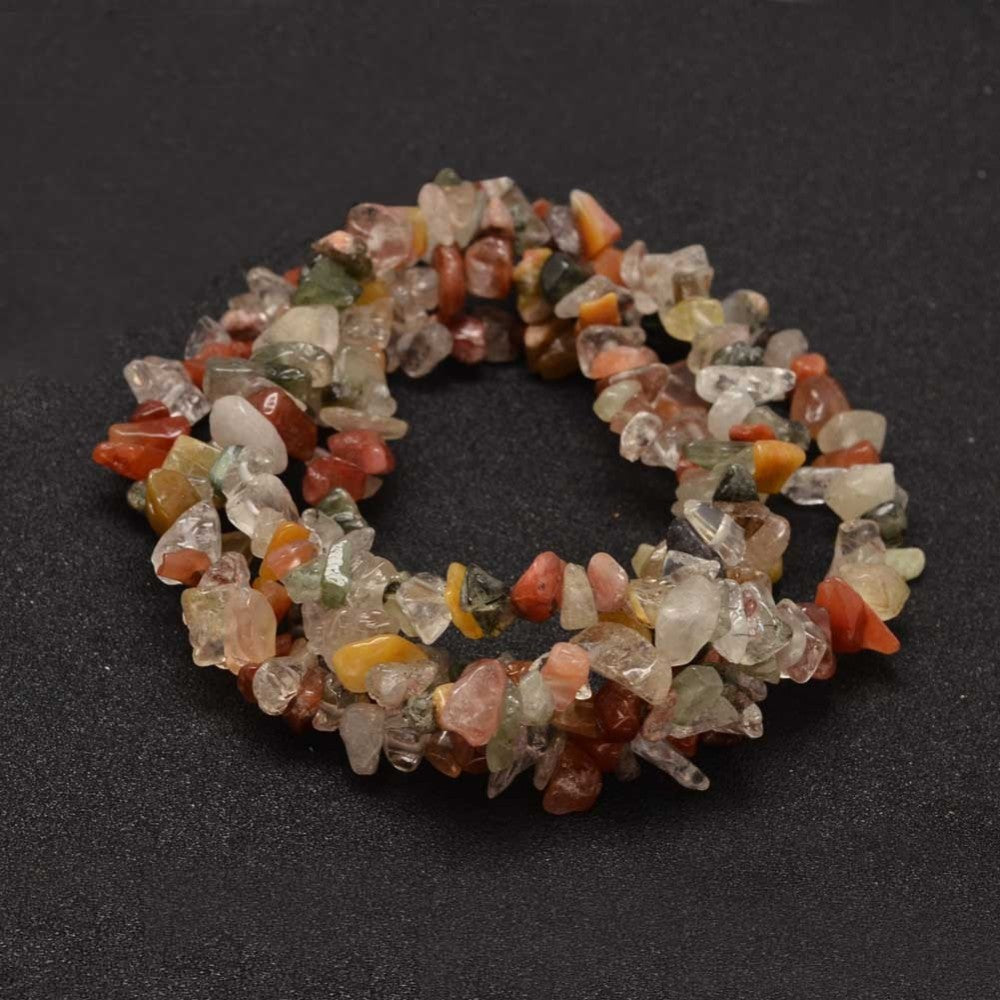 multi-color rutilated quartz chip bead strand in swirl design over black surface. 