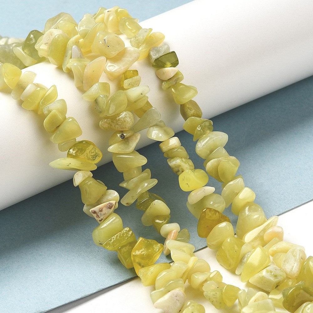 four lemon jade chip bead strands draped over white cylinder onto light blue and white surface. 