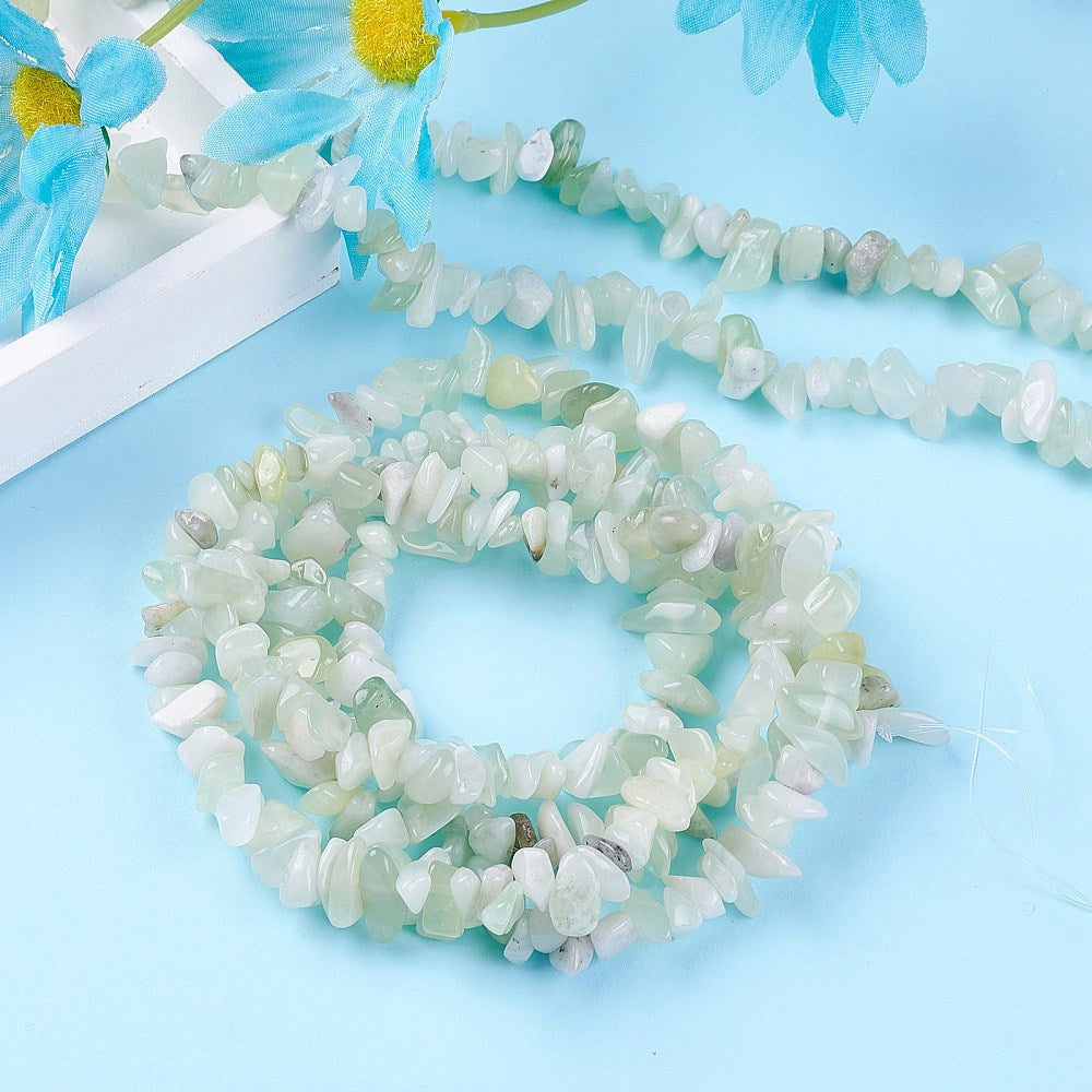 multiple strands new jade chip bead strands displayed over light blue surface with a white tray and bright blue daisy flowers peeking in from the corner.