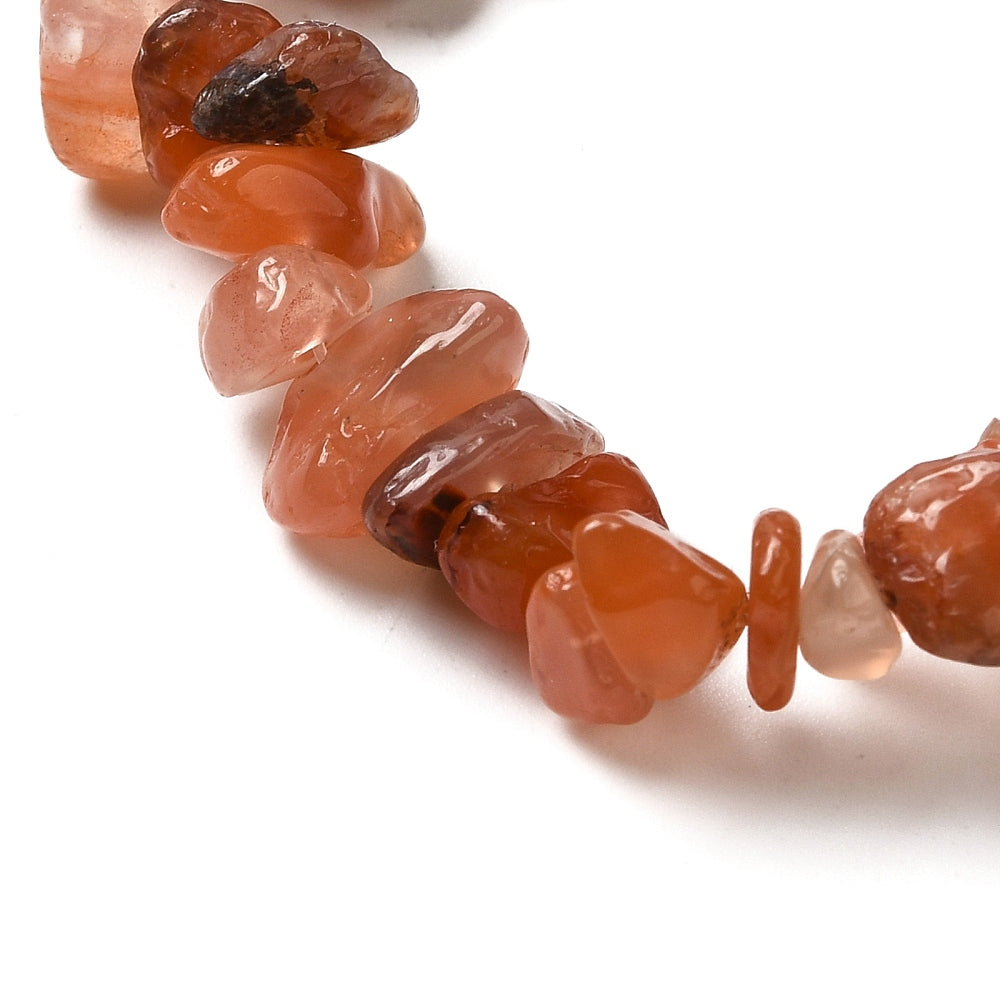 zoomed in section of red agate chip bead strand over white background. 