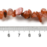 zoomed in section of red agate chip strand displayed above a ruler over white surface. 