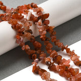 four red agate chip bead strands draped over white cylinder on grey and white surface.