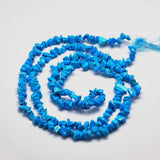 dyed light sky blue synthetic turquoise chip bead strand in a swirl design over white surface. 