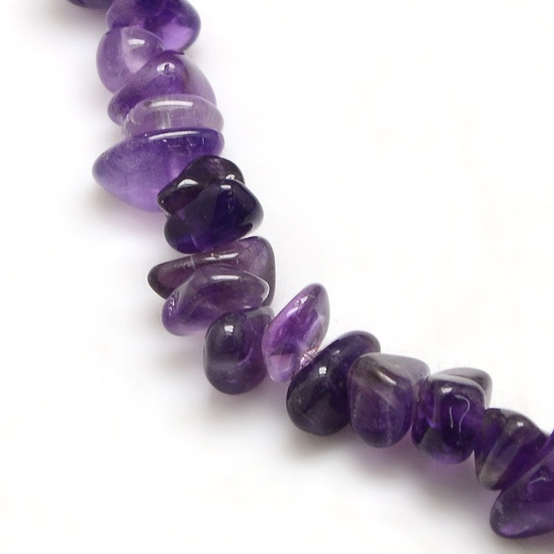 zoomed in sections of dark purple tumbled amethyst chip bead strand over white surface. 