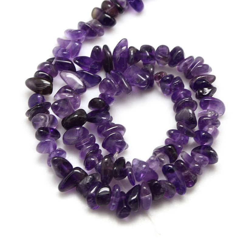 dark purple tumbled amethyst chip bead strand in swirl design over white surface. 