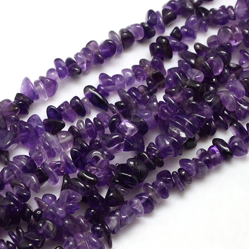zoomed in sections of dark purple tumbled amethyst chip bead strand over white surface. 