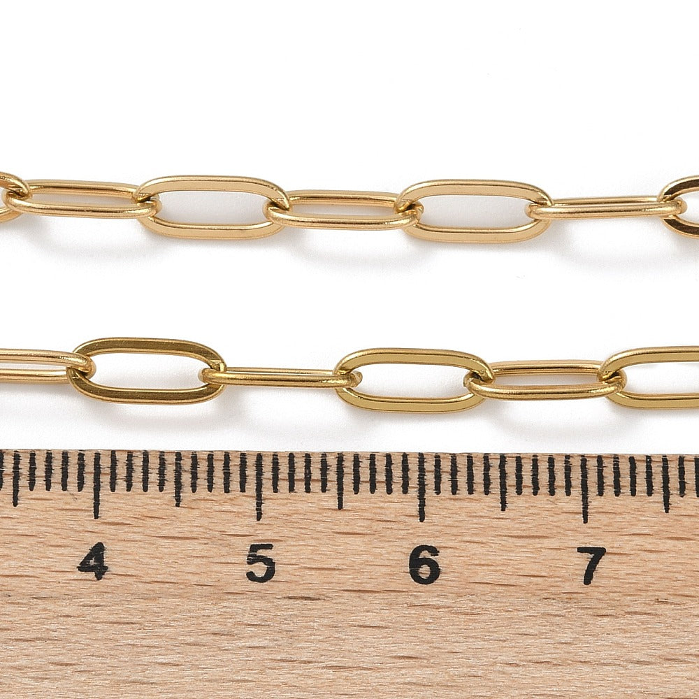 golden paperclip chain necklace displayed above wooden ruler over white background. 