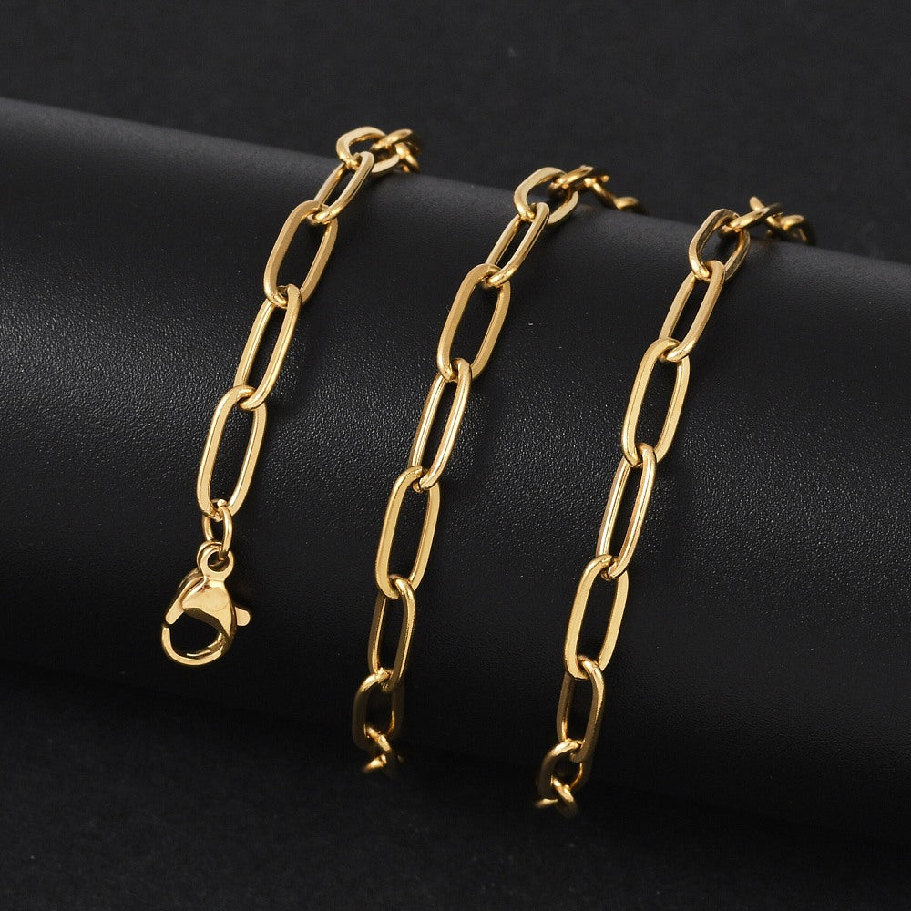 golden paperclip chain necklace with lobster claw clasp wrapped around black cylinder form with black background. 