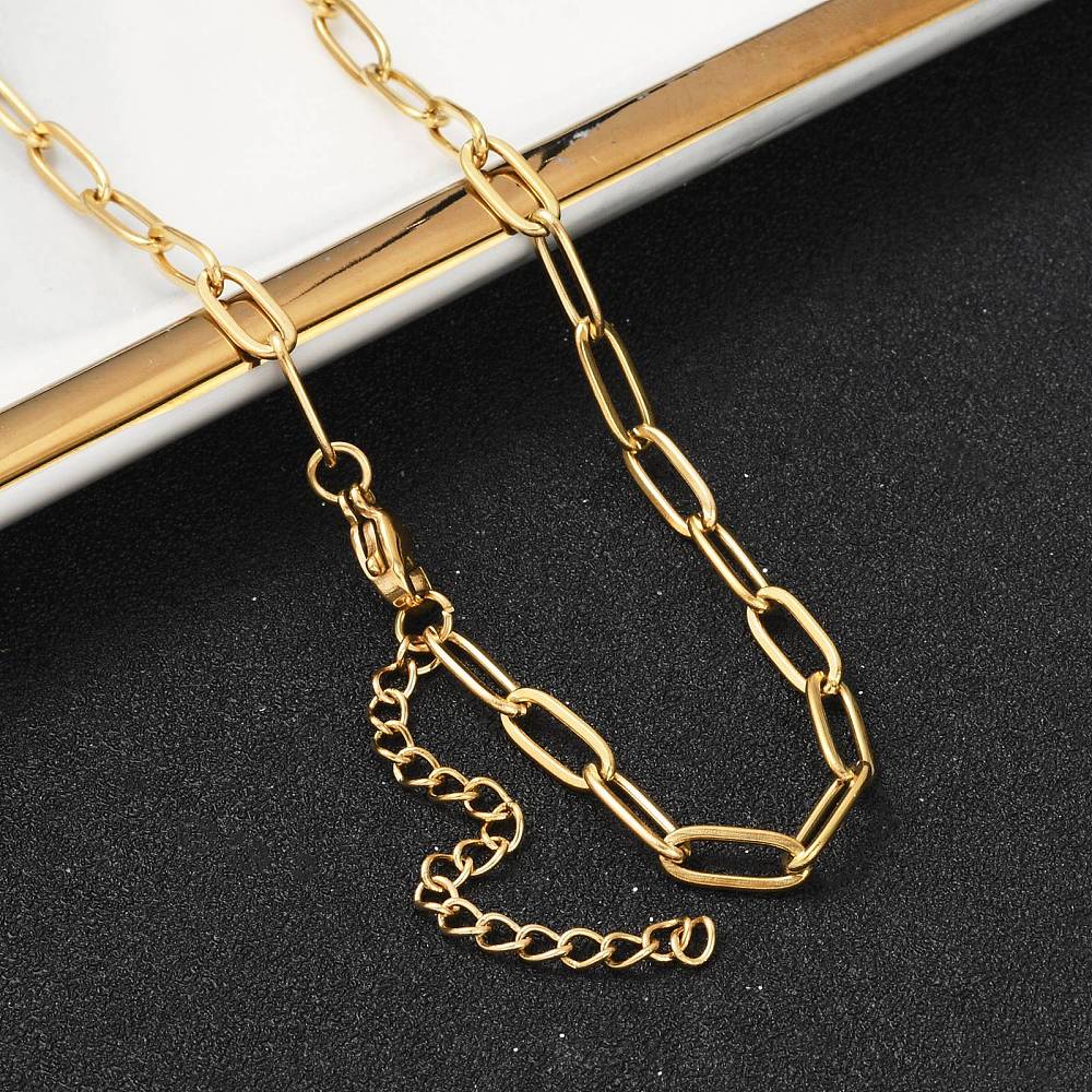 golden paperclip chain necklace with lobster claw clasp and extender chain draped over gold rimmed tray edge onto black textured surface. 