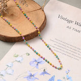 golden multi-color enamel twisted chain necklace  draped over tree trunk slice onto piece of paper with writing and  watercolor flowers. 