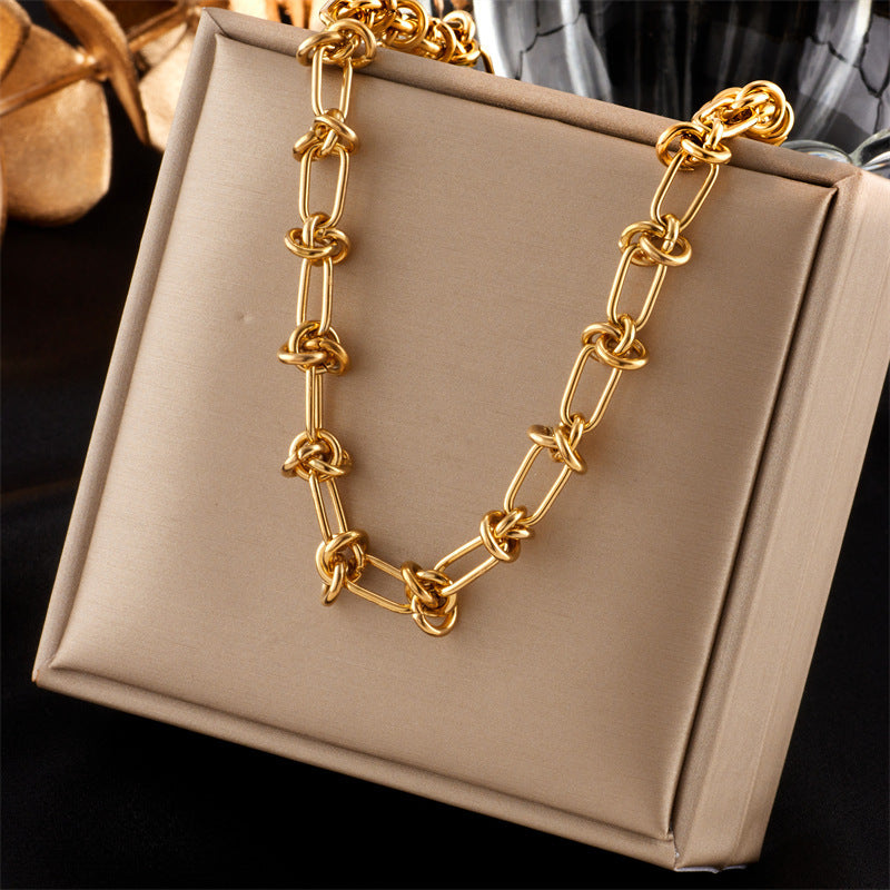 golden knotted paperclip link necklace displayed over a tan box with a black and grey background. 