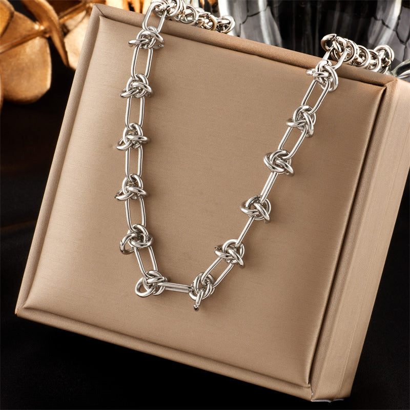 silver tone knotted paperclip link necklace displayed over a tan box with a black and grey background. 