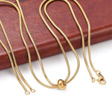 golden snake chain bolo necklace with lobster slider stopper bead lobster claw clasp and jump rings draped over edge of brown leather book onto white surface.  
