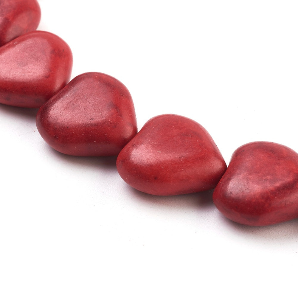 zoomed in section of dyed red howlite heart bead strand over white surface. 
