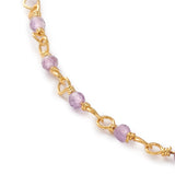 zoomed in section of golden chain and purple amethyst faceted round beaded necklace over white background. 