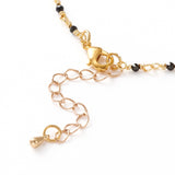 zoomed in section of golden chain and black spinel faceted round beaded necklace with golden lobster claw clasp and extender chain over white background. 